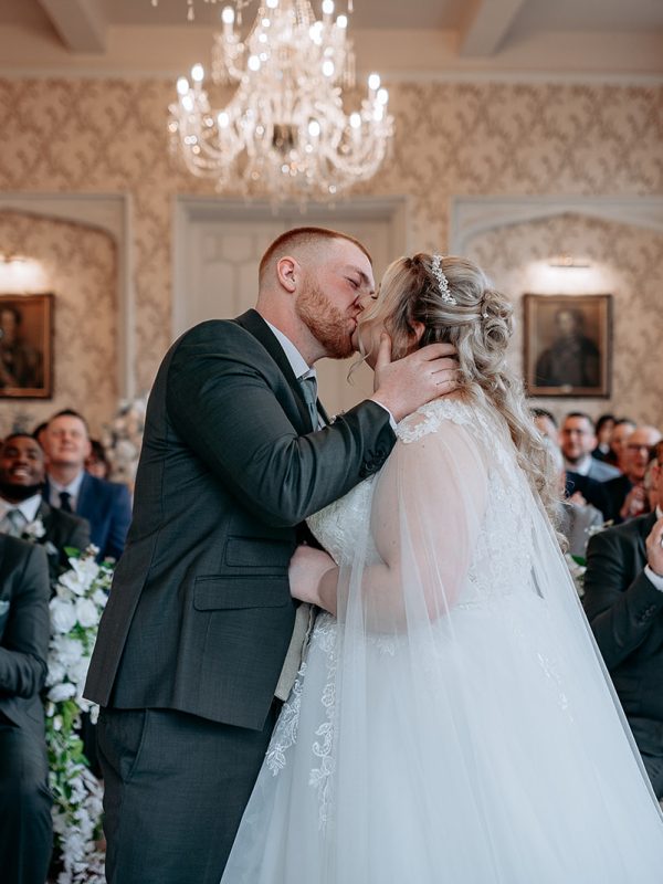 Bride and groom first kiss surrounded by guests at Rowton Castle