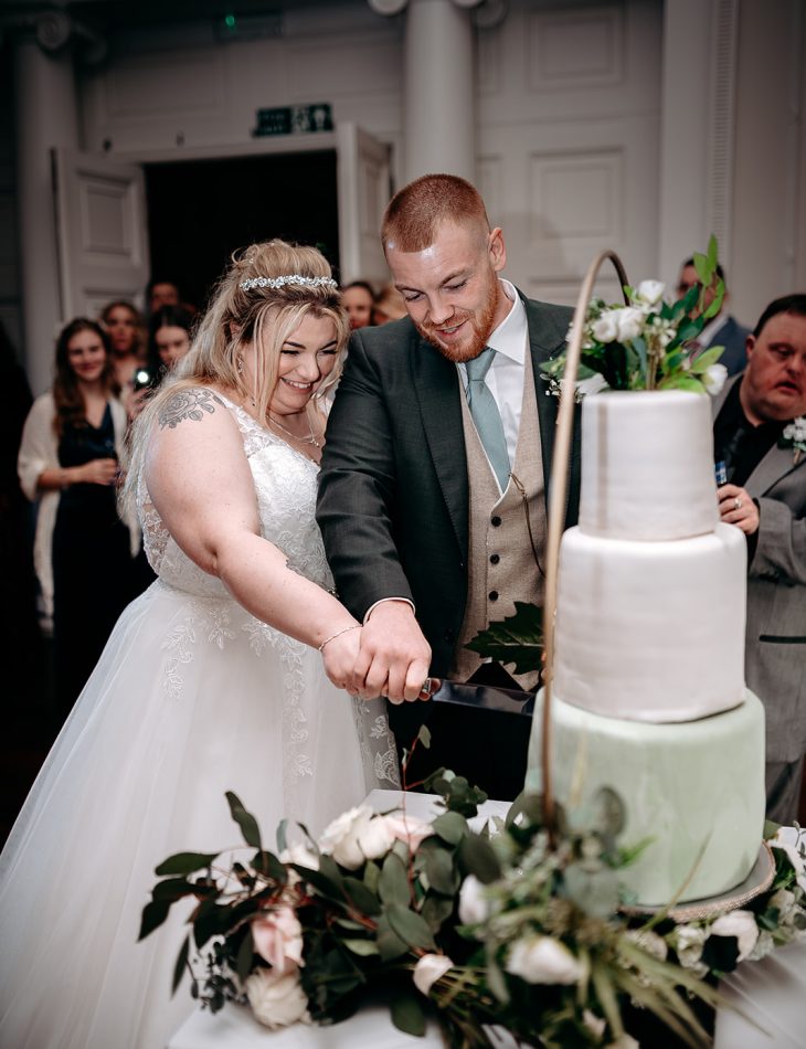 Bride and groom cutting cake surrounded by guests at Rowton Castle